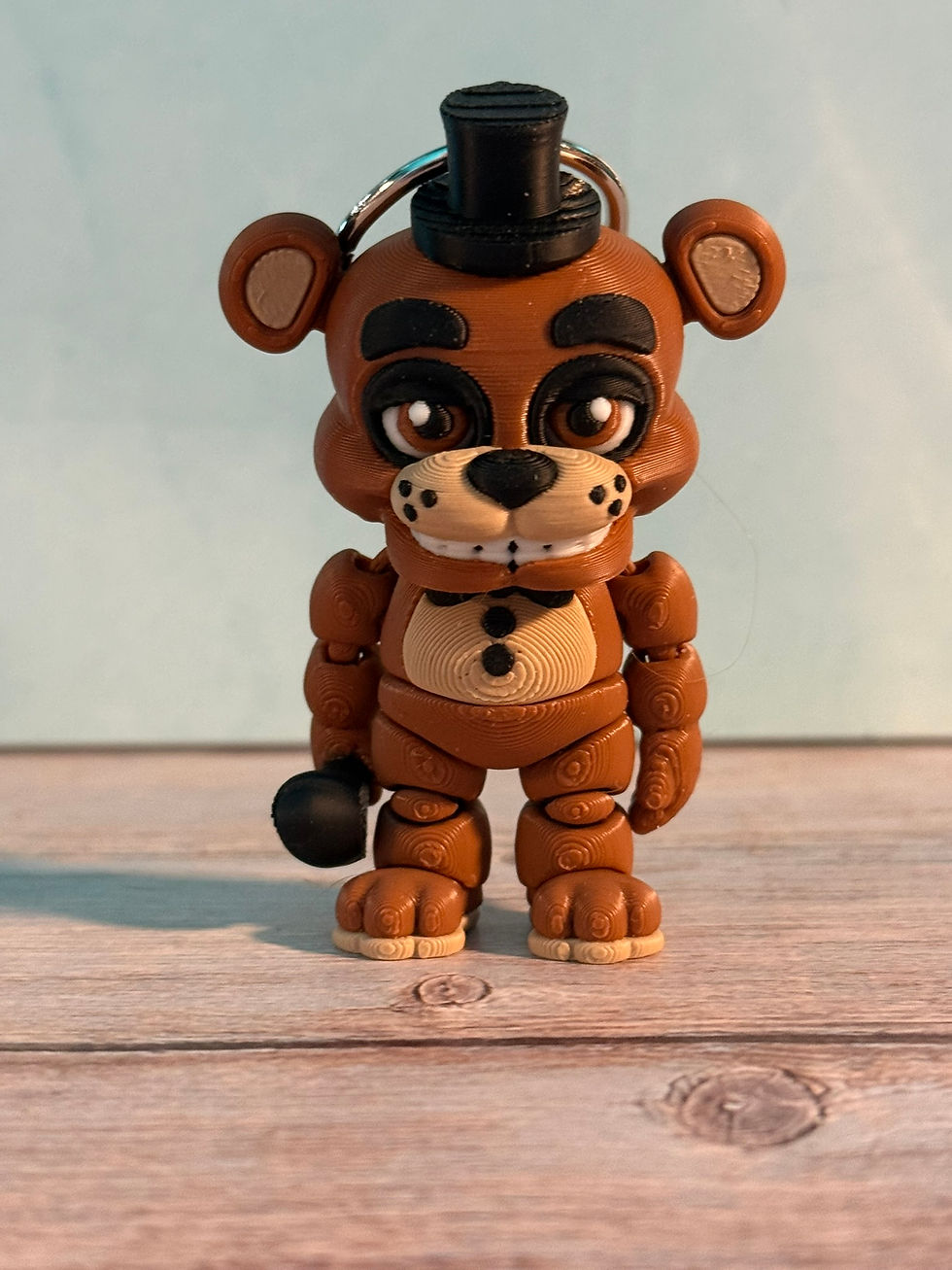 Thumbnail: Brown animatronic-style bear keychain with a black top hat and microphone standing on a black-and-white checkered floor with 