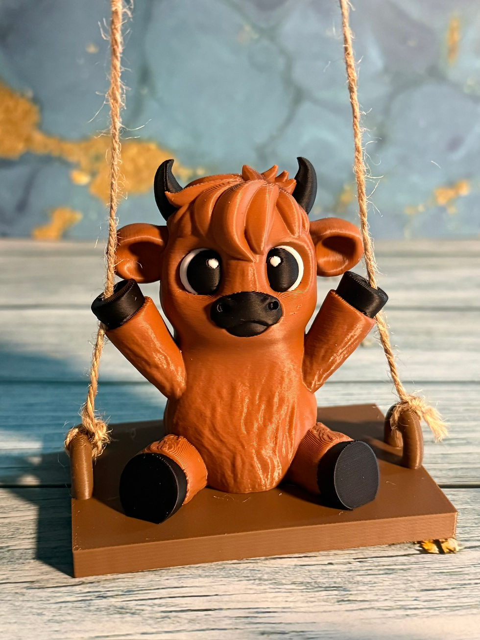 Thumbnail: Cute 3D printed brown cow figurine sitting on a rope swing with oversized black eyes and tiny horns