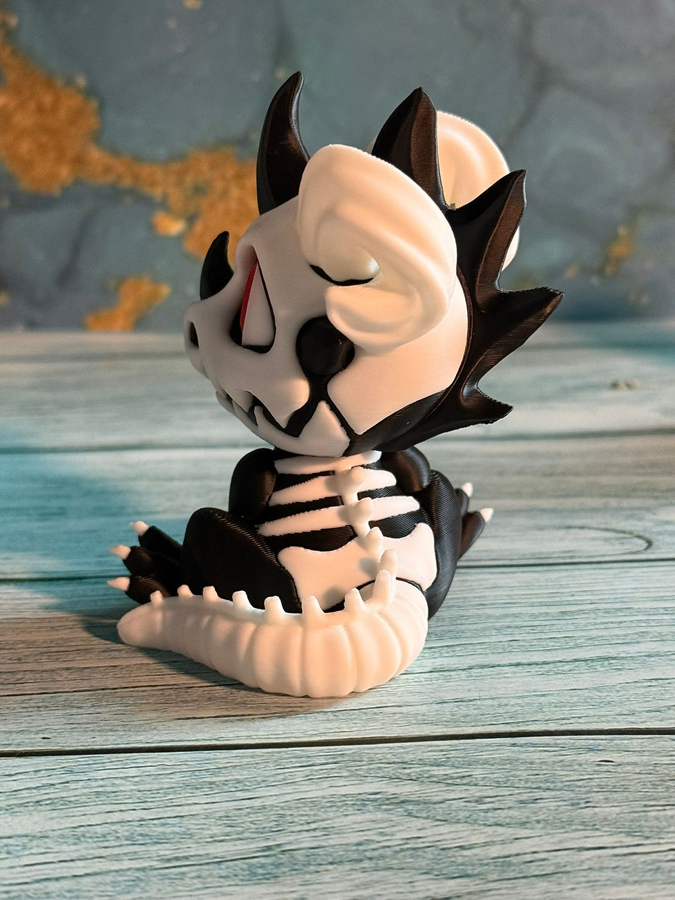 Cute black and white skeleton baby dragon figurine with red eyes, horns, and skeletal details sitting beside a tiny skull
