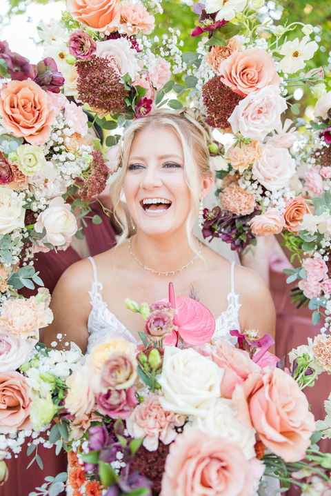 Bride laughing with vibrant bouquets of coral, blush, and burgundy roses. Chicago suburbs wedding florist.