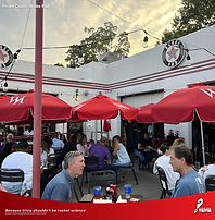 Outdoor trivia night at Brake Pad in College Park GA with players under red umbrellas enjoying food, drinks, and team trivia fun.