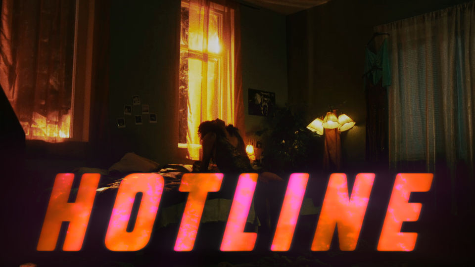 film still, drag queen sitting on the side of his bed looking up at the ceiling, the text "HOTLINE" is overlayed over the picture