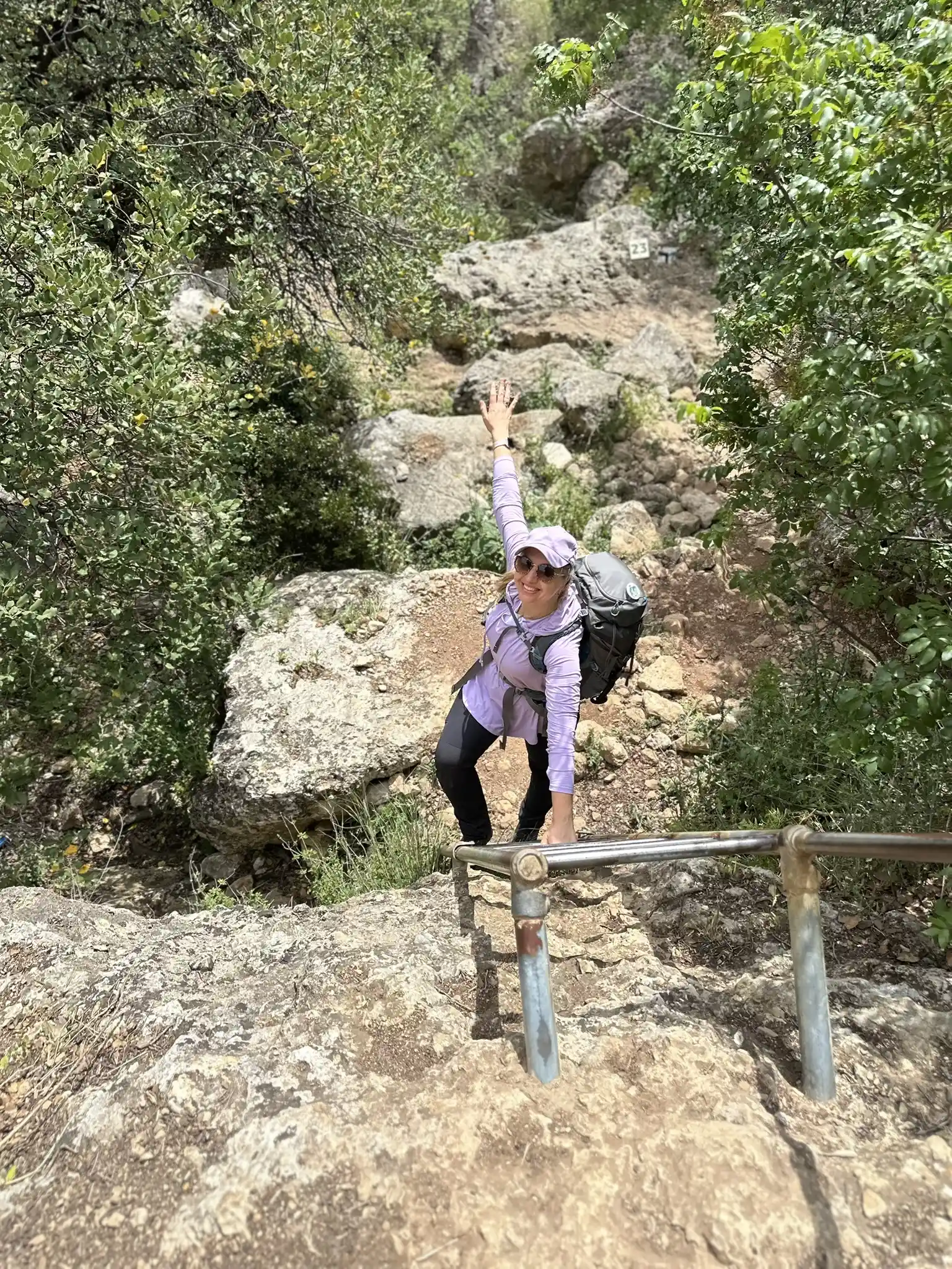 девушка с рюкзаком спускается со скалы по лестнице