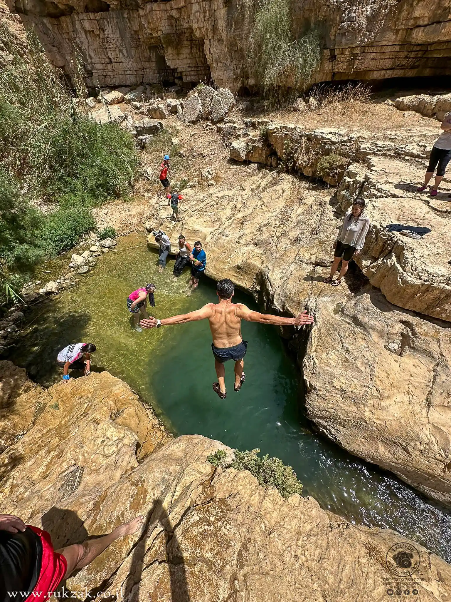 мужчина прыгает со скалы в воду источника