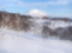 Snow-covered hills in front of a snowcapped Mount Yotei partially covered by clouds in Niseko, Japan