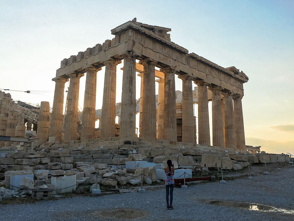 Eryn standing in front of the ruined bricks and columns of the Parthenon of Athens at sunset