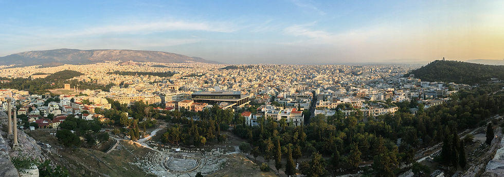 A panoramic view of buildings in the city of Athens, the Theater of Dionysus, and the Acropolis Museum, and surrounding greenery from the top of the Acropolis