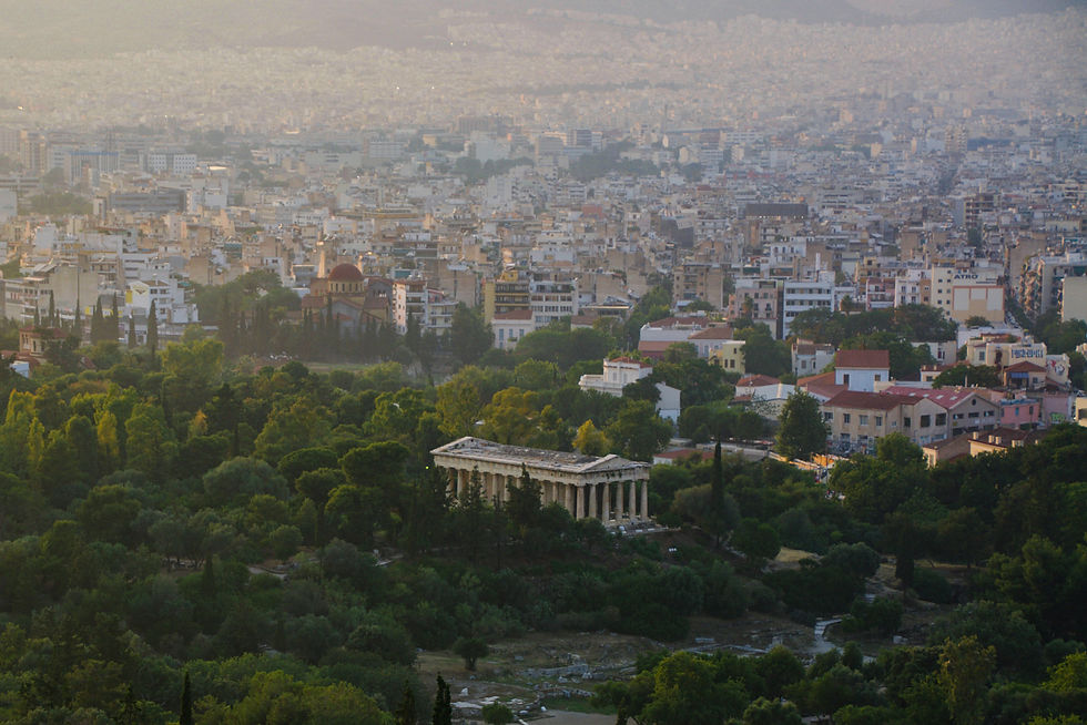 An ancient structure amid the greenery of a park with the city of Athens in the distance