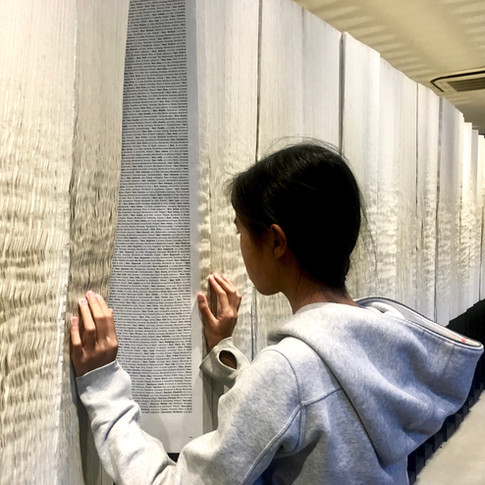 Eryn looks at a page of the Book of Names standing vertically and stretching across a hall in Auschwitz