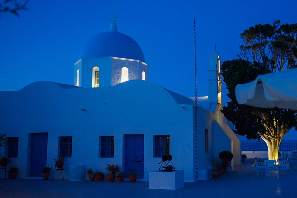 Everything turns dark blue as night sets in while yellow lights illuminate the inside of the church's blue dome and the underside of a tree in Aghios Artemios