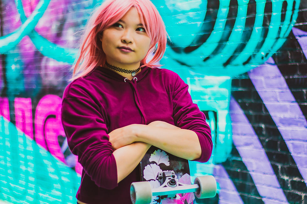 Person with pink hair and a burgundy sweatshirt holding a skateboard