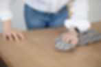 A woman wiping a light oak table with a black and white linen cloth