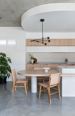 Interior Design photography of an oak kitchen with pink leather chairs and decorative plaster and concrete finishes. A contemporary black pendant over a curved table height island bench extension.