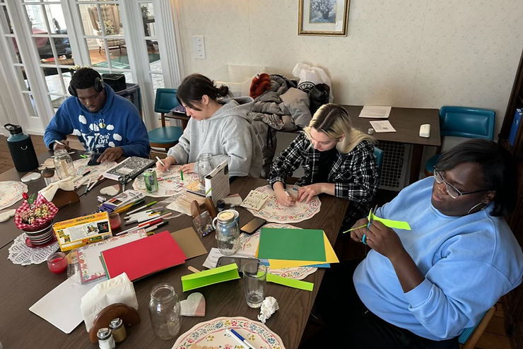 Four people sit around a table laden with crafting supplies, engaged in their work.