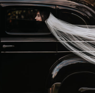 Velo de novia volando sobre auto clásico negro con la novia visible a través de la ventana, fotografía artística de boda por Christian Macías, fotógrafo de bodas en Guadalajara, Jalisco.