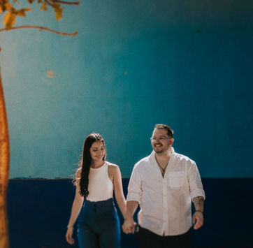 Pareja caminando de la mano frente a pared azul en sesión de compromiso, fotografía de engagement en Guadalajara por Christian Macías, fotógrafo de bodas en Jalisco.