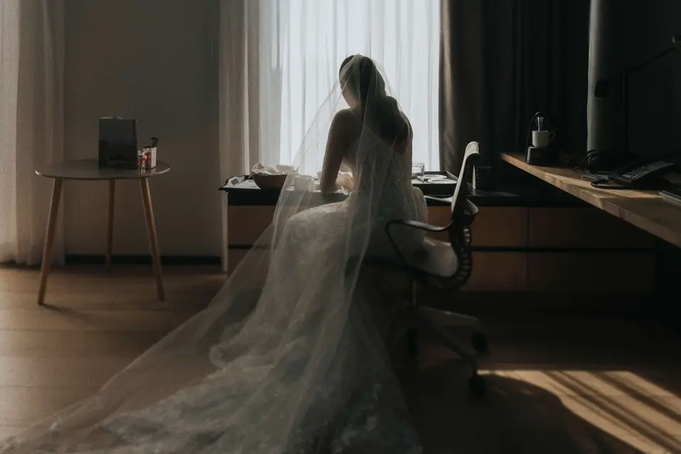 Novia de espaldas con velo largo frente a ventana, momento íntimo antes de la ceremonia, fotografía documental de bodas