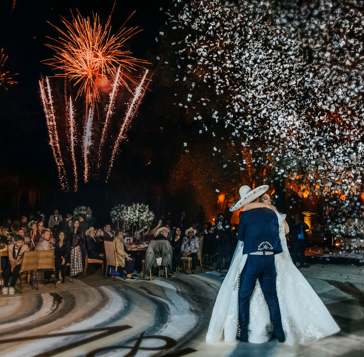 Pareja celebrando con explosión de papel picado, fondo de escenario elegante.