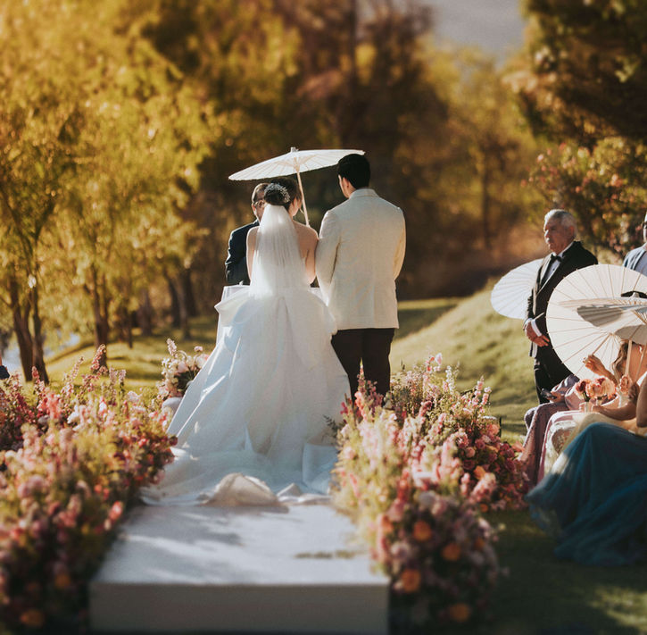 Ceremonia de boda al aire libre con pasillo de flores rosas y sombrillas blancas en jardín de Jalisco, fotografía documental