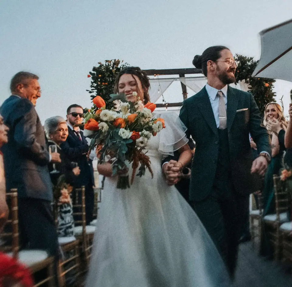 Novios recién casados saliendo del altar en ceremonia al aire libre rodeados de invitados aplaudiendo, fotografía documental de boda por Christian Macías, fotógrafo de bodas en Guadalajara, Jalisco.