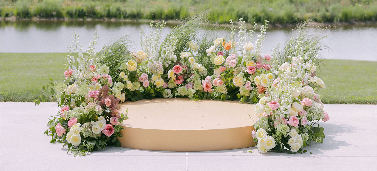 Light and bright summer wedding ceremony set up with circular stage and meadow arrangements