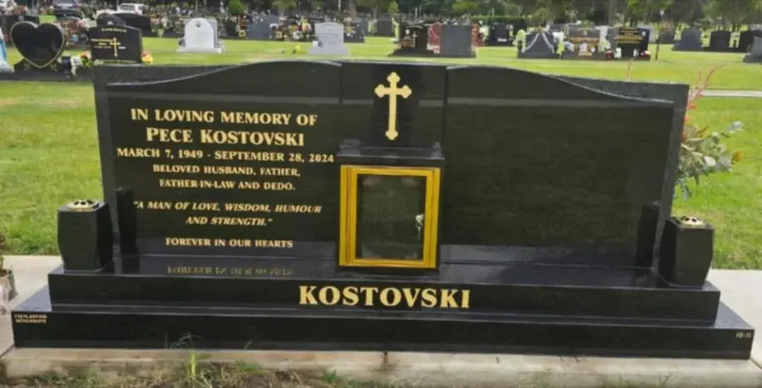 Black granite headstone with gold text and cross.