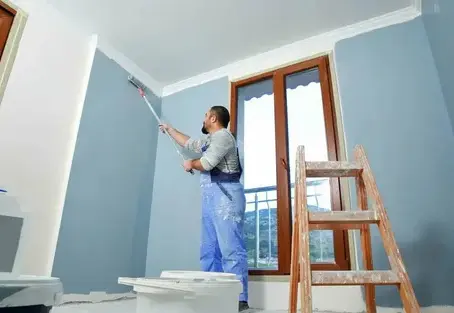Painter applying blue paint on interior wall with roller.