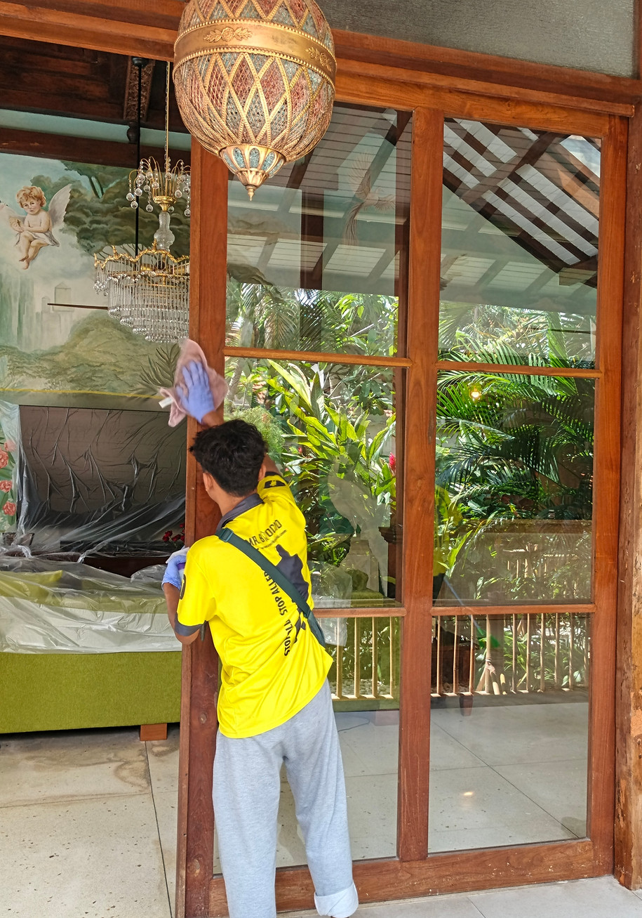 Mr. Biocid technician removing mold from a large wooden glass door in a Bali villa during treatment.