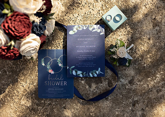 Invitiation surrounded by boutonniere, bouquet, and wedding bands/rings.