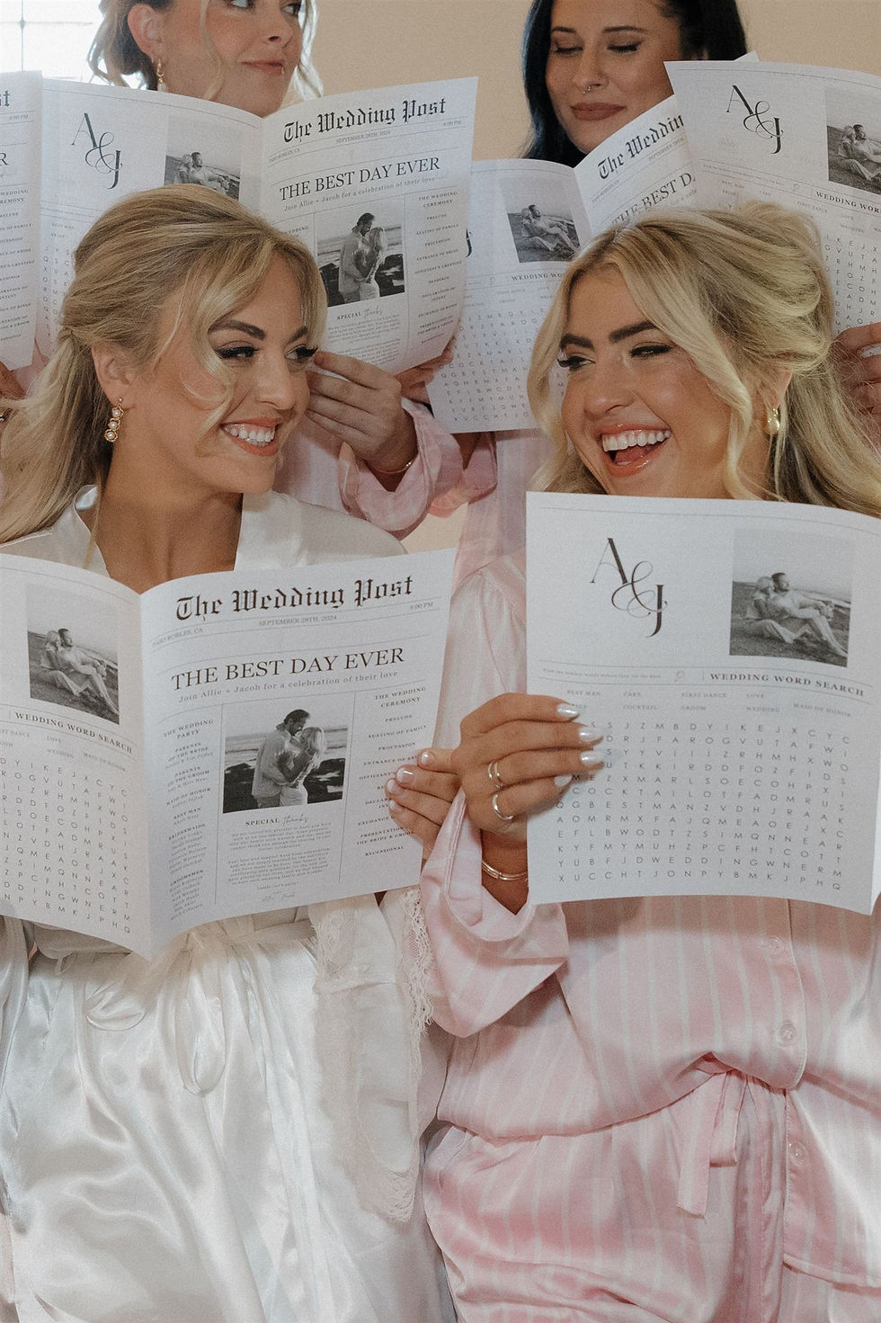 Bridesmaids in pink robes joyfully read personalized newspapers titled "The Wedding Post" with "The Best Day Ever" headline.