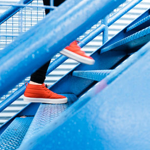 Person in red shoes climbing blue metal stairs, with a striped background and wet railing, suggesting a fresh, vibrant scene.