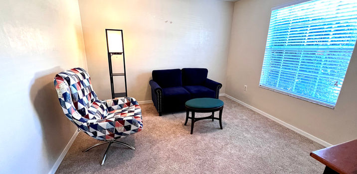Cozy living room with blue couch, patterned chair, small table and window.