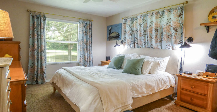 Bedroom with bed, curtains, window, and nightstands featuring floral patterns and decor.