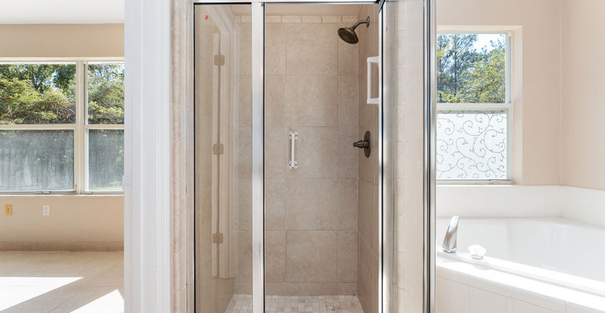 Modern bathroom with glass shower door, shower head and beige tiles.