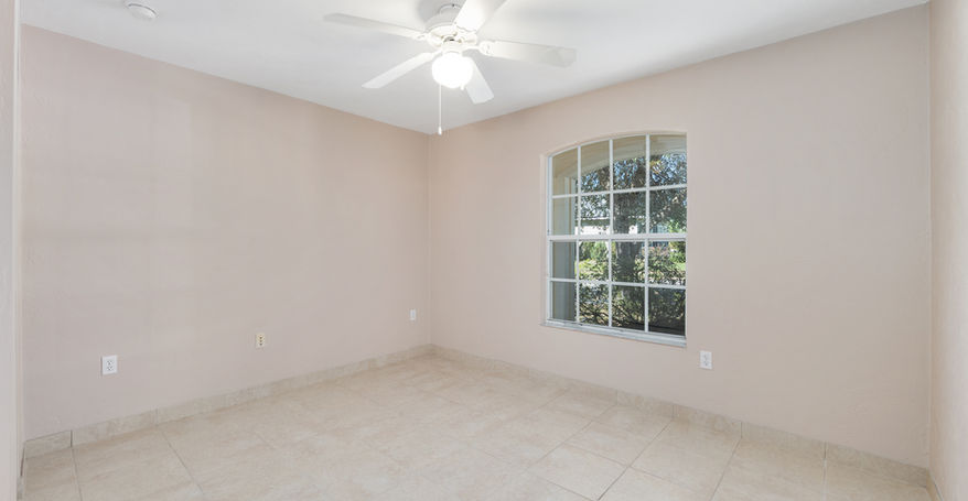 Empty room with tile floor and a window overlooking greenery and a ceiling fan.