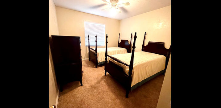 Two beds in bedroom with dark furniture and ceiling fan
