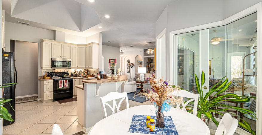 Bright dining room with a table, chairs, flowers, and open kitchen layout.