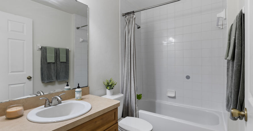 Bathroom with sink, tub, toilet, towels; neutral tones with bright lighting.