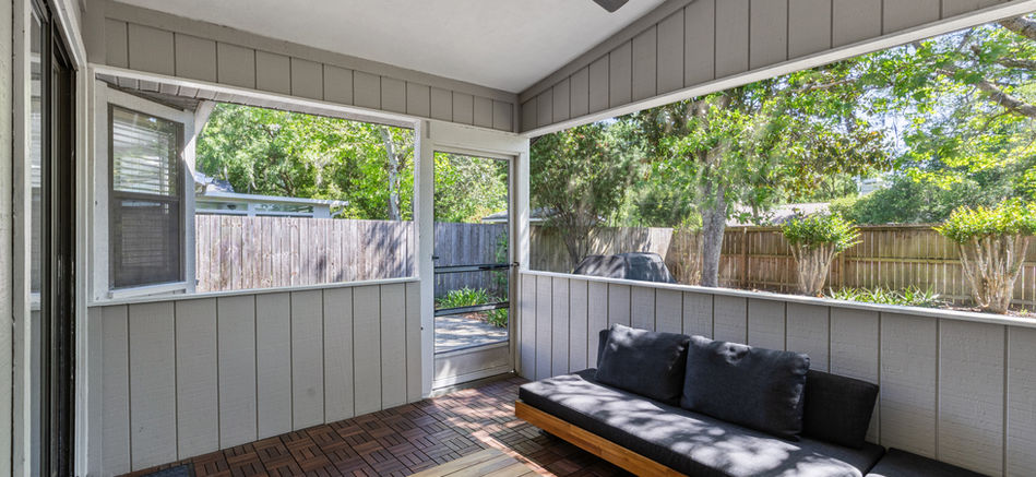 Outdoor living space with sofa, coffee table, and open windows, nature view.