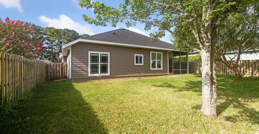 Backyard view of house with windows, lawn, and fence; sunny day.