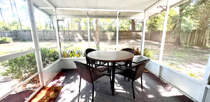 Patio with round table and chairs surrounded by screens with backyard view.