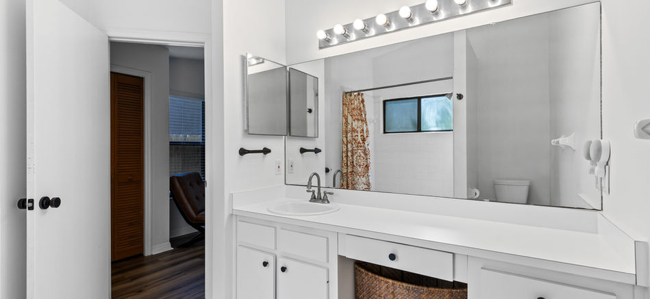 White bathroom with mirror, sink, cabinets, window, and decorative lighting fixtures.