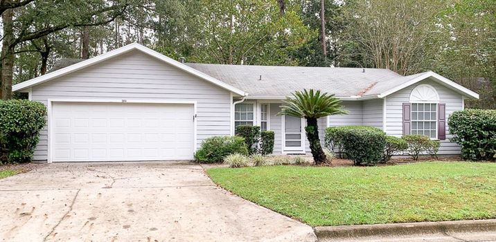 Residential home with a white garage door surrounded by greenery on the lawn.