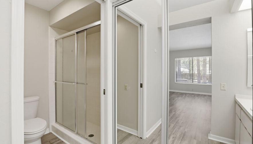 Bathroom with toilet, glass shower, mirrored closet, wood floor