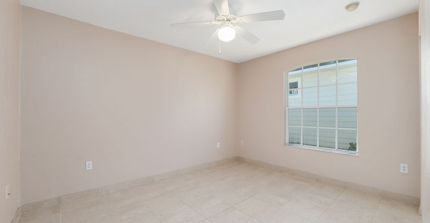 Empty bedroom with a ceiling fan, window, and tile floor, ready for buyers.