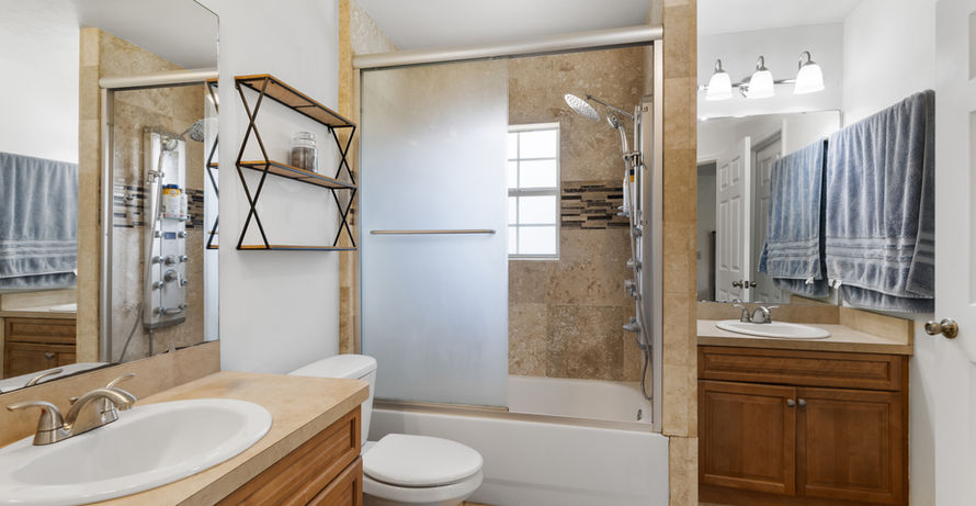 Bathroom with a shower, toilet, and sink. Beige tile and neutral decor.
