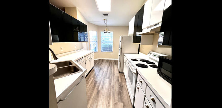 Modern kitchen with white cabinets, appliances, and wooden floor details.