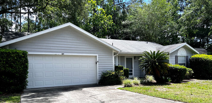 Exterior view of a house with a garage and driveway surrounded by nature.