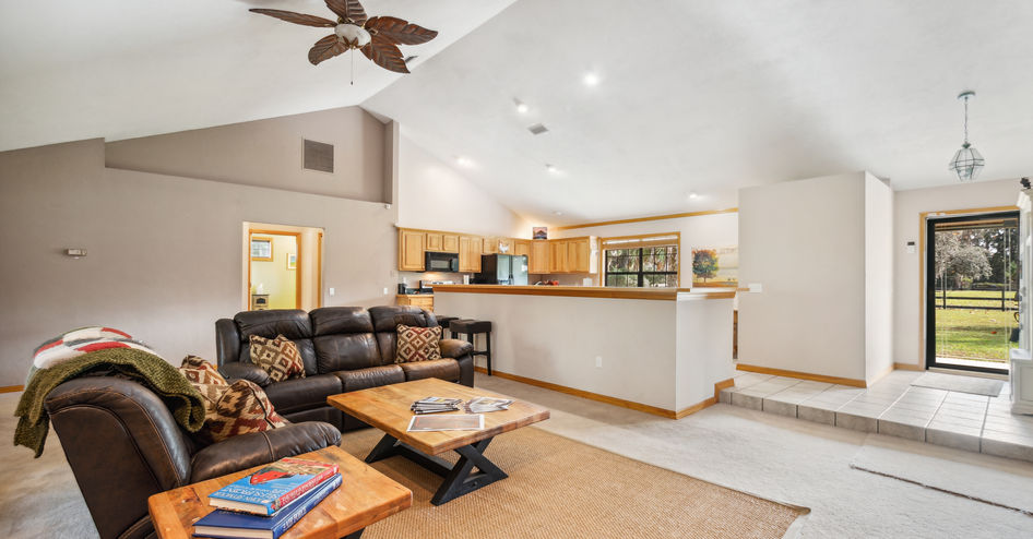 Cozy living room with black leather sofa, wooden tables, and open kitchen space.