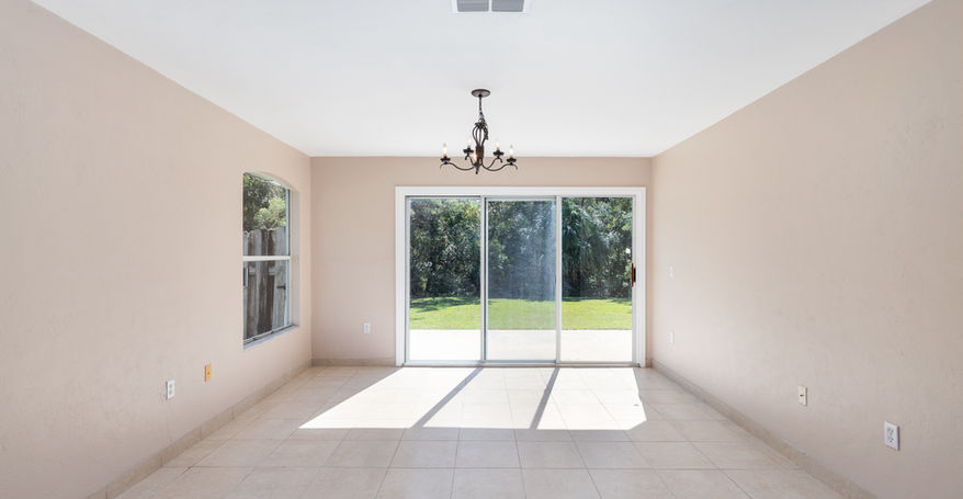 Empty room with sliding glass door, chandelier and outside view.